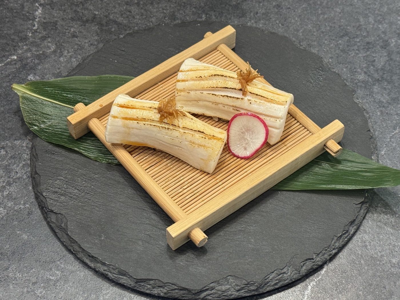 Two lightly seared pieces of nigiri on a bamboo tray with a radish garnish
