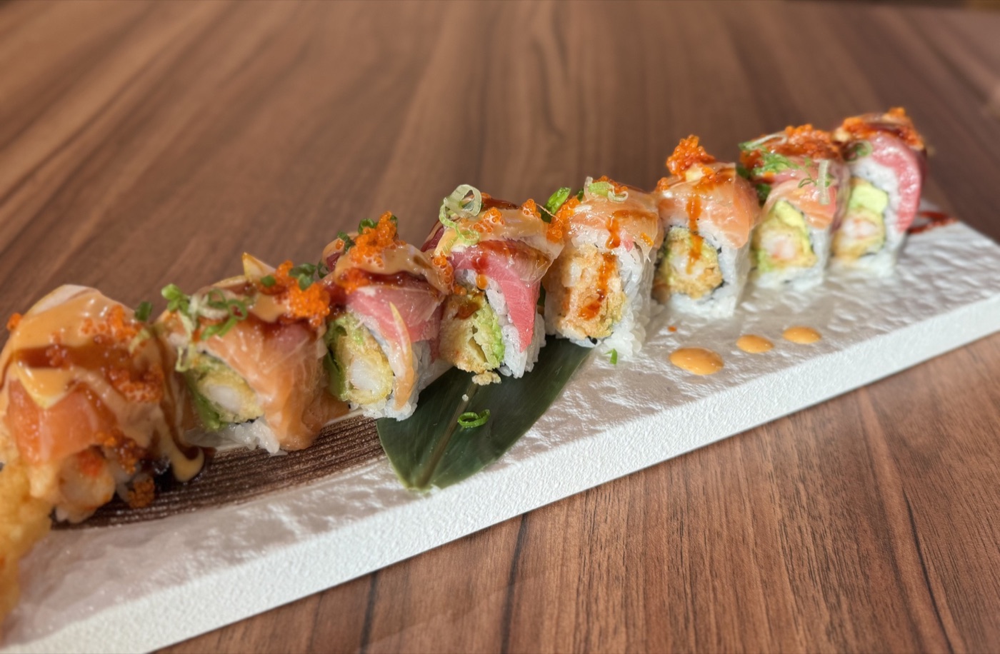 A colorful sushi roll arranged diagonally across a long white ceramic plate