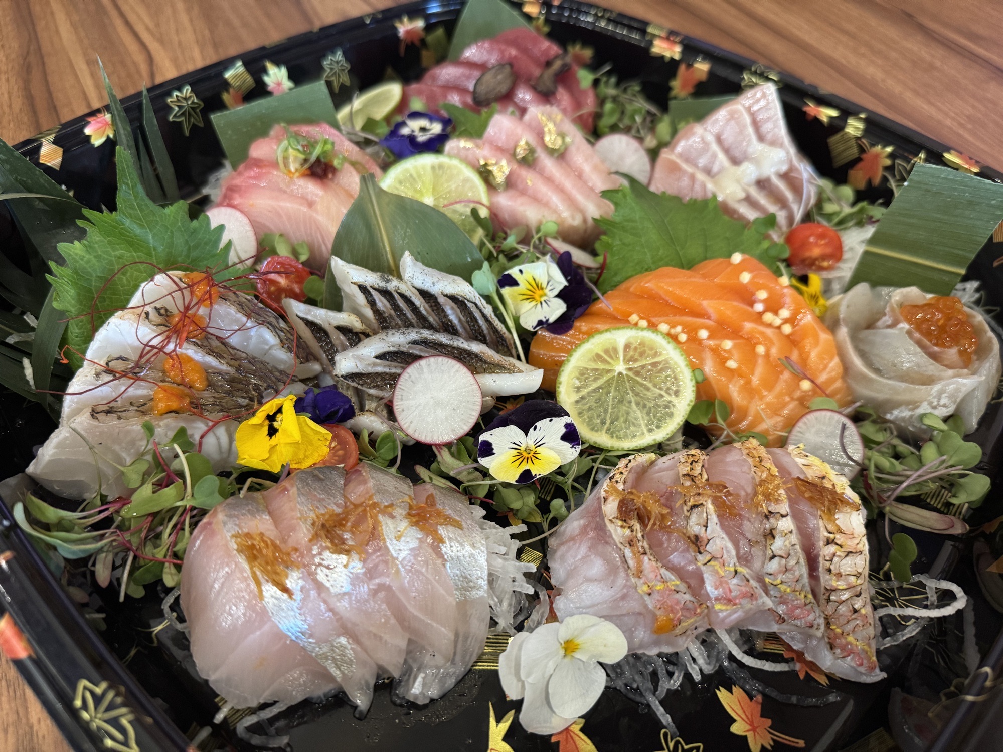 Assorted sashimi with citrus slices, radishes, green leaves, and small flowers