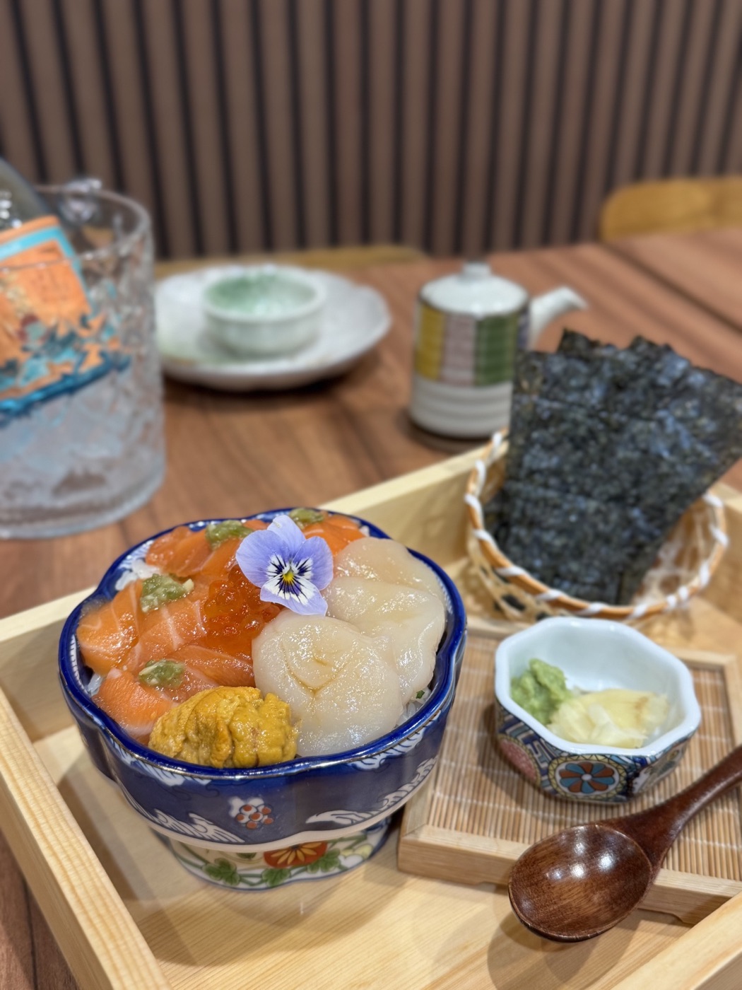 A seafood bowl with salmon, scallops, sea urchin, and a flower, served with seaweed and condiments