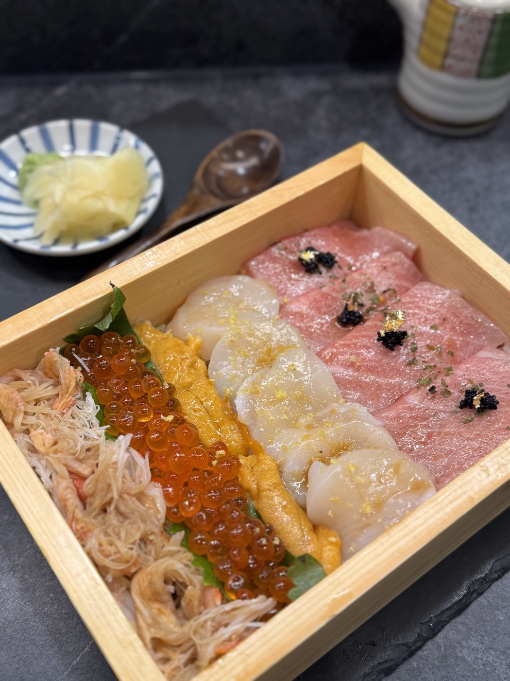 Assorted seafood arranged in rows in a wooden box, with roe, scallops, and pink fish