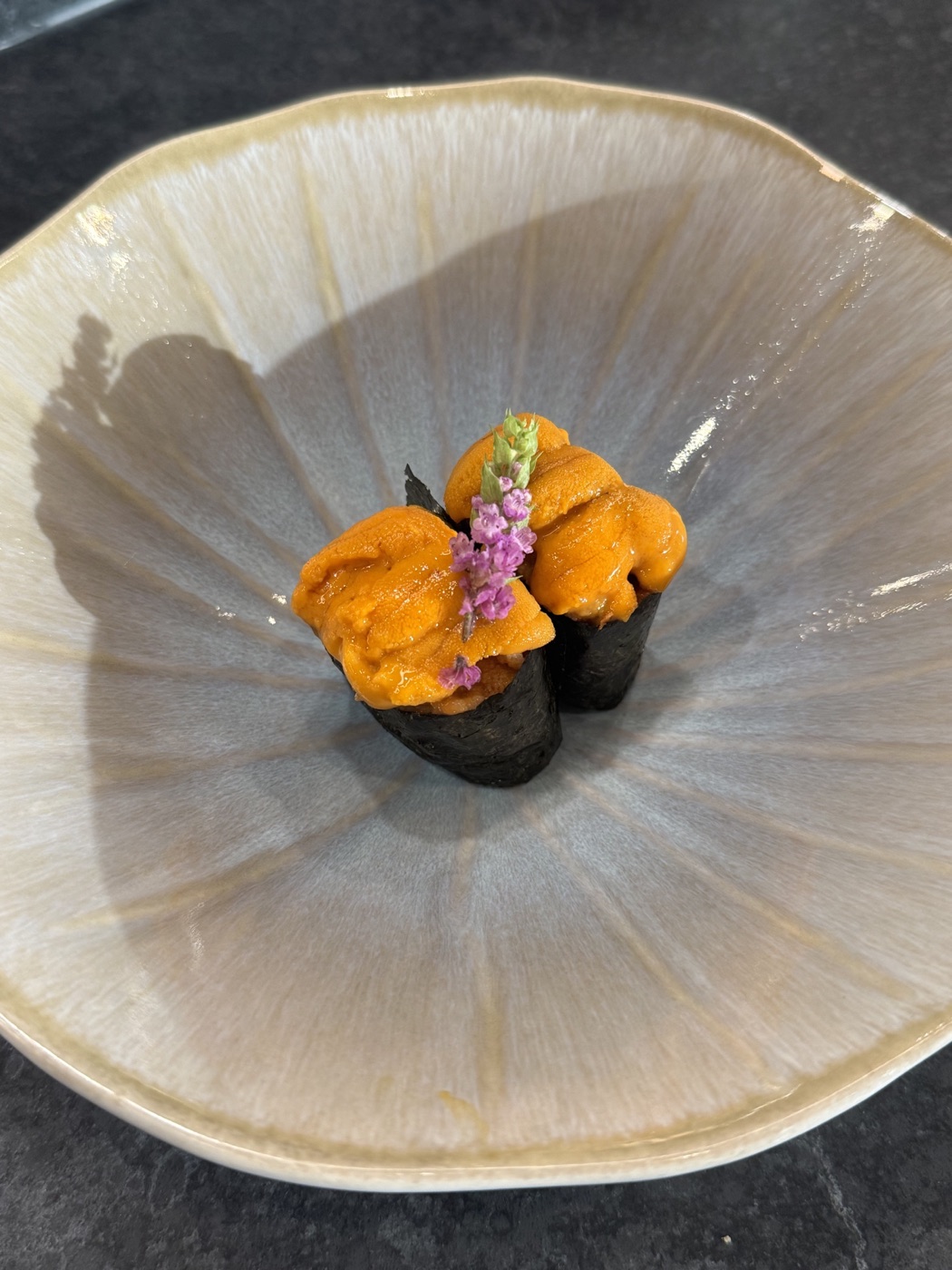 Two sea urchin sushi pieces with a purple flower in a pearly ceramic bowl